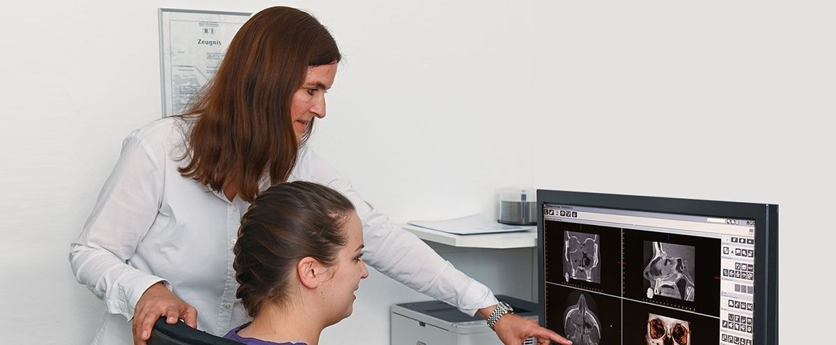 Eine Ärztin zeigt einer Patientin Röntgenaufnahmen am Bildschirm und erklärt die Ergebnisse.