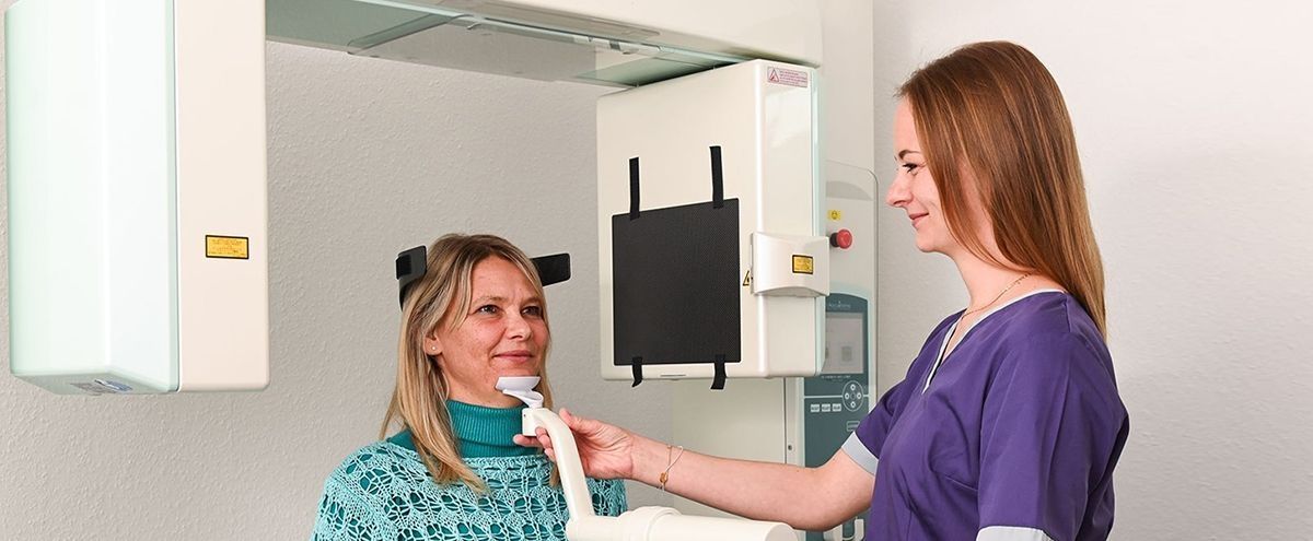 Eine Frau wird von einer medizinischen Fachkraft für eine zahnmedizinische Röntgenaufnahme positioniert.