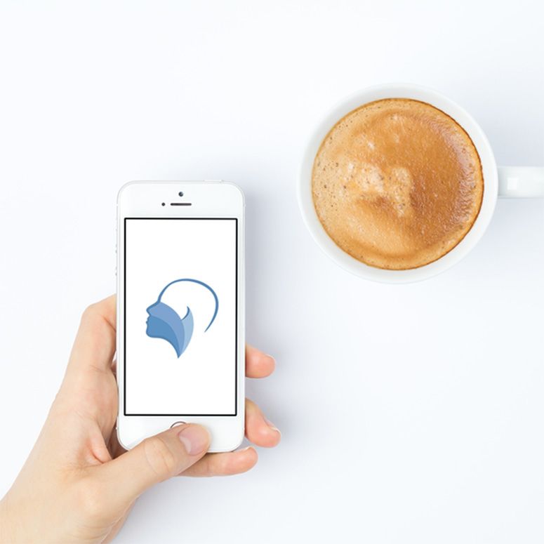 Hand hält ein Smartphone mit einem Logo, daneben eine Tasse Cappuccino auf einem weißen Hintergrund.